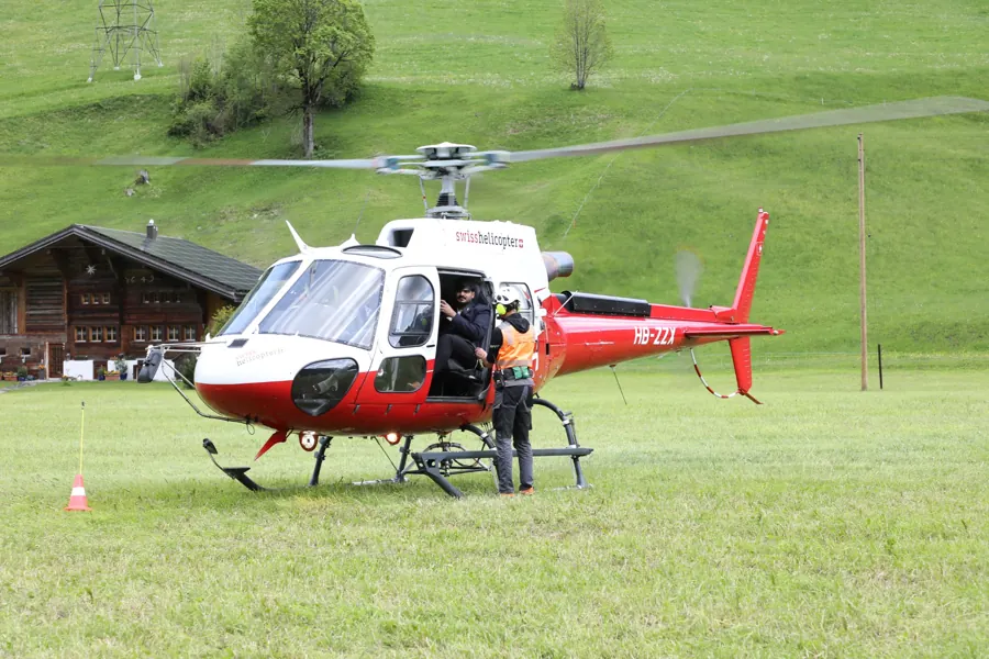 Guests boarding a red and white helicopter on an Alpine meadow